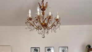 Un dormitorio con cama, candelabro, obras de arte enmarcadas en la pared y mesita de noche con lámpara.