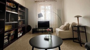 Una sala de estar con sofá, mesa de centro, estantería, televisor y lámpara.