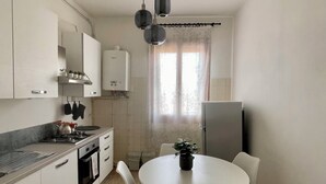 Una cocina compacta con comedor, muebles blancos, estufa y lámpara en el techo.
