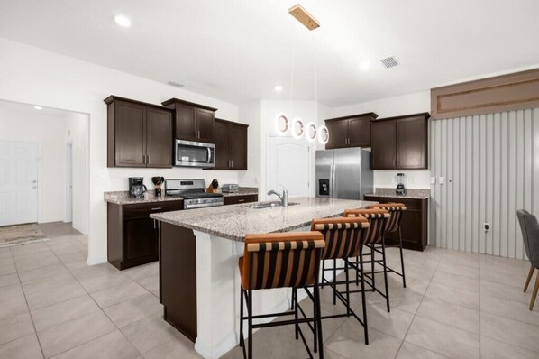 A modern kitchen with dark cabinets, stainless steel appliances, a granite countertop island with bar stools, and a white door.