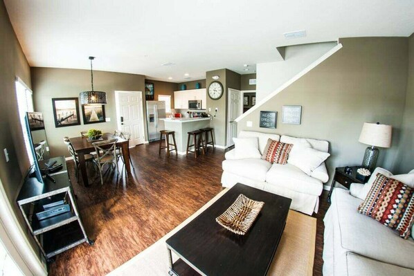 A modern living room with a black coffee table, white sofas, and a dining area with a kitchen in the background.