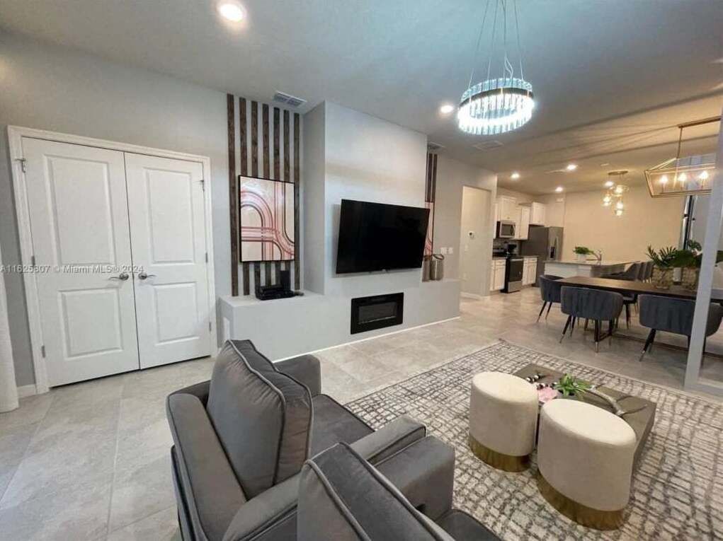 A modern living room with a grey sofa, ottoman, and a flat-screen TV mounted on the wall.