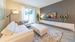 A modern living room with a sofa, ottoman, and a TV mounted on the wall.