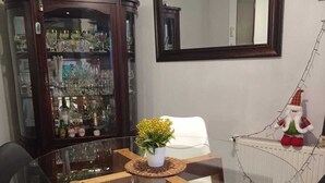 A dining area with a glass-top table surrounded by chairs, a cabinet with glassware, a mirror, and a small decorative gnome.