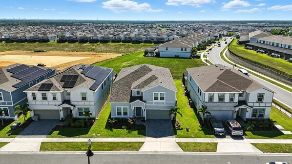 A residential area with houses featuring solar panels, a clear road, and a distant view of more houses.