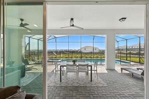 Uma área de pátio moderna com estrutura de vidro, piscina e mesa de jantar com cadeiras.