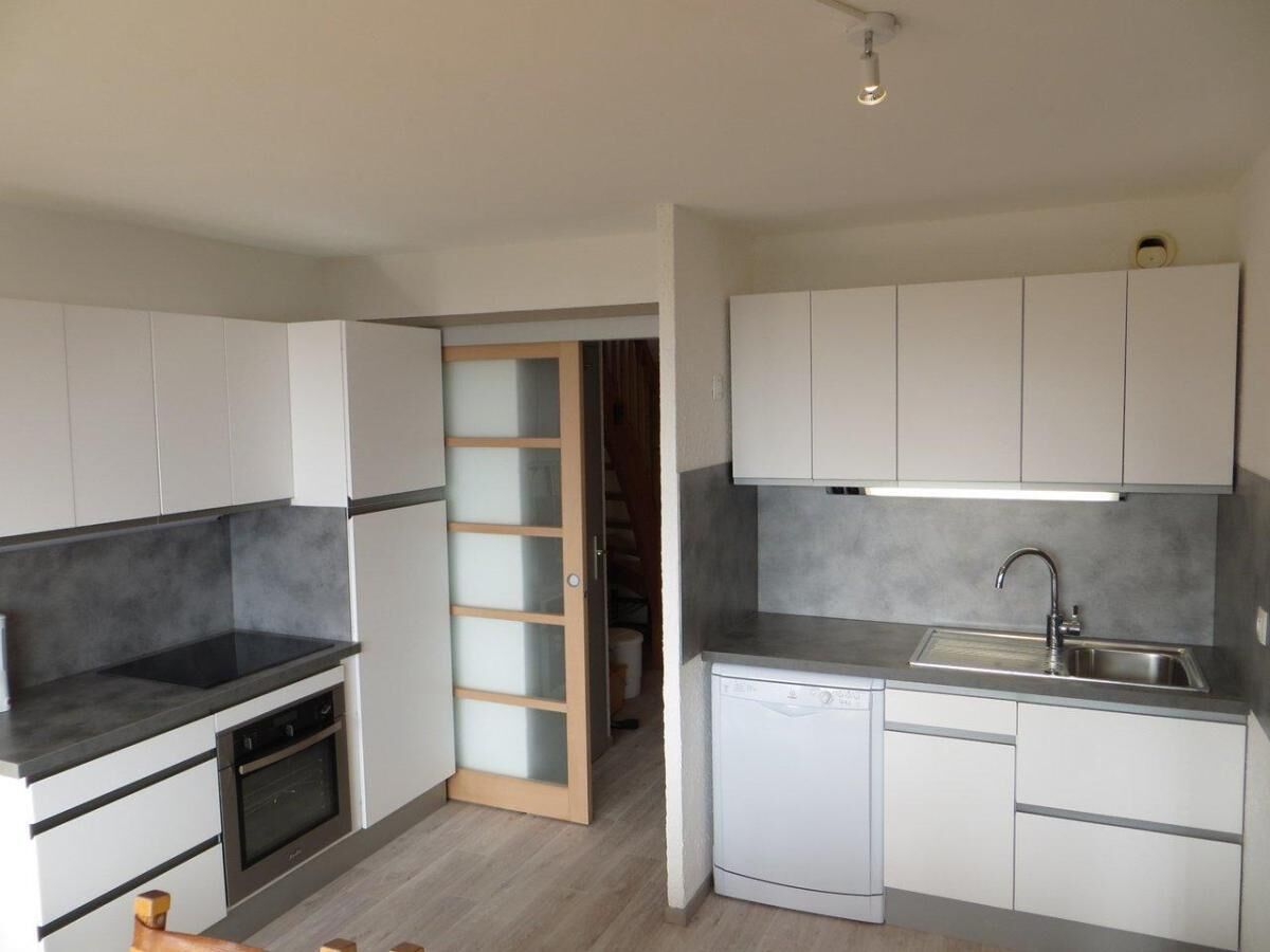 A compact kitchen with white cabinets, a black countertop, a built-in oven, and a dishwasher.