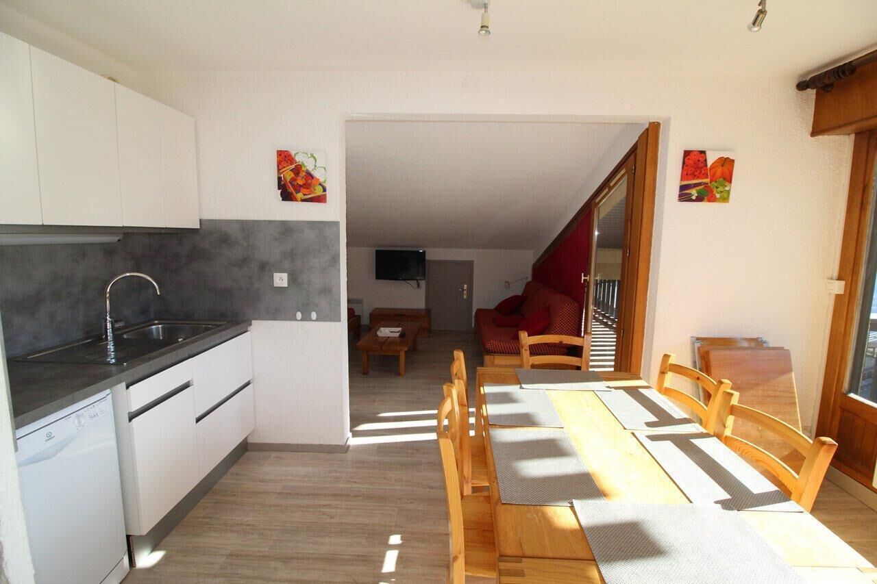 Een functionele keuken met een vaatwasser, een eethoek met een houten tafel en stoelen, en een zithoek met een bank en een televisie.