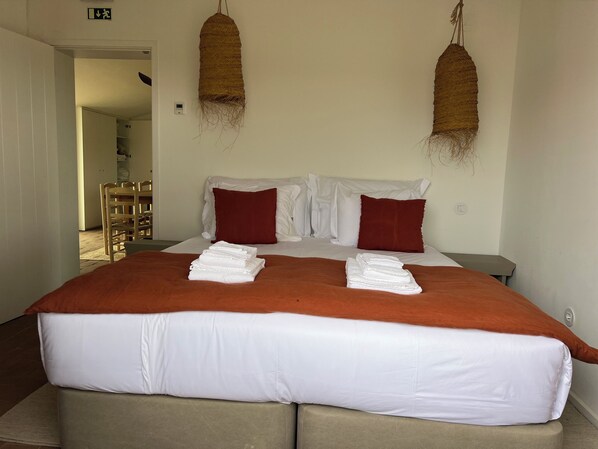 A hotel room with a large bed, two red pillows, a brown throw blanket, and two woven wall hangings. - Monte das Casolas (Grandola)