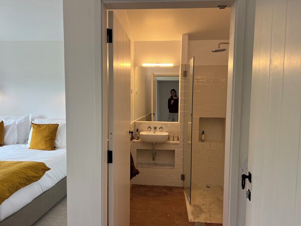 A hotel room with a bed, a bathroom with a sink, and a shower. - Monte das Casolas (Grandola)