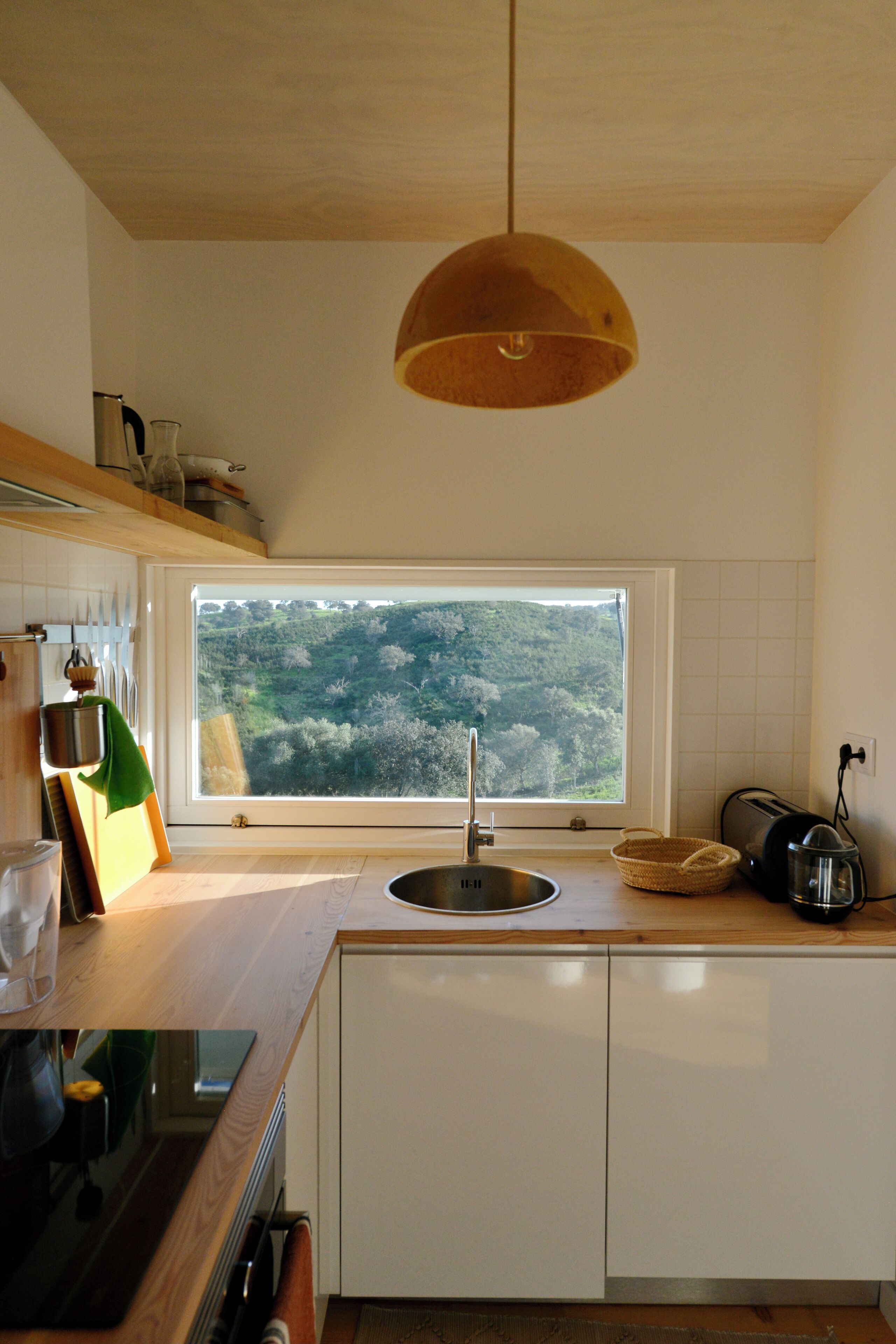 A kitchen with a window, wooden cabinets, a sink, and a hanging light fixture.