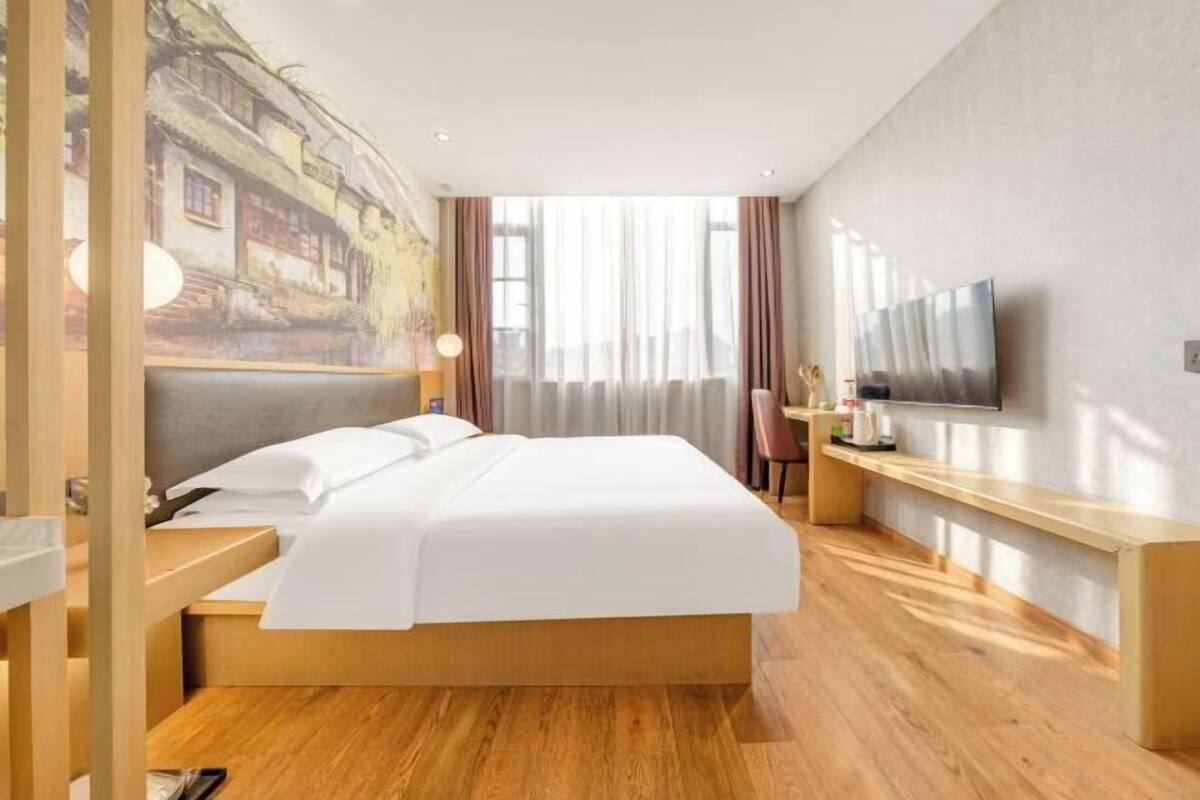 A hotel room with a bed, a desk, a chair, a TV, and a large window with curtains.