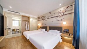 Une chambre d’hôtel avec un plancher en bois, deux lits, une table de chevet, un miroir, un porte-peignoir et un mur décoré de motifs représentant des branches.