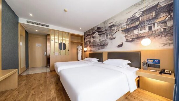 Une chambre d’hôtel avec un grand lit, un téléviseur fixé au mur, une table de chevet avec une lampe et une fresque représentant des éléments d’architecture traditionnelle.