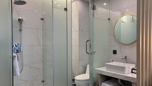 Une salle de bain moderne avec une douche à parois de verre, des toilettes blanches et un lavabo blanc avec un miroir au-dessus.