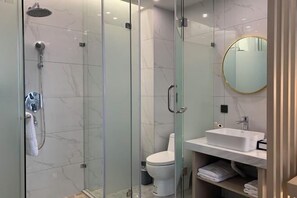 A modern bathroom with a glass-enclosed shower, a white toilet, and a white sink with a mirror above it.