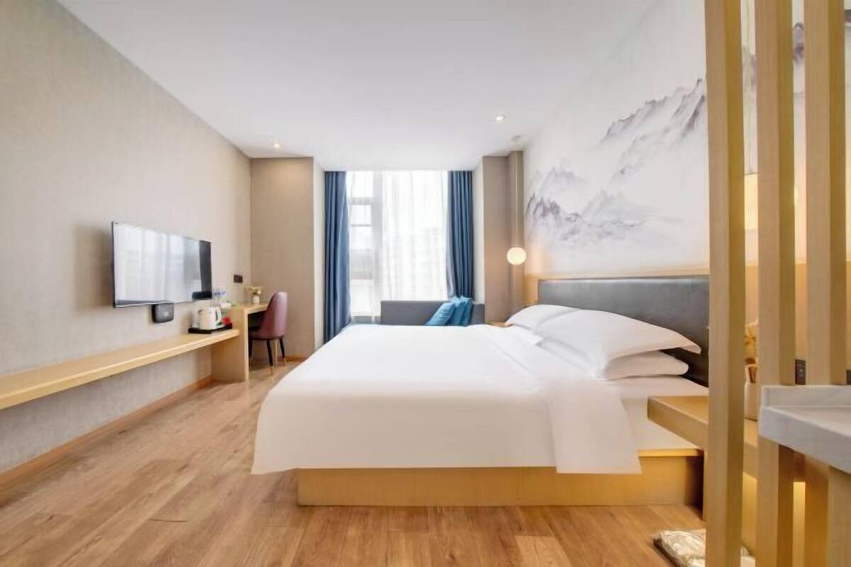 A hotel room with a bed, a television, a desk, and a window with curtains.