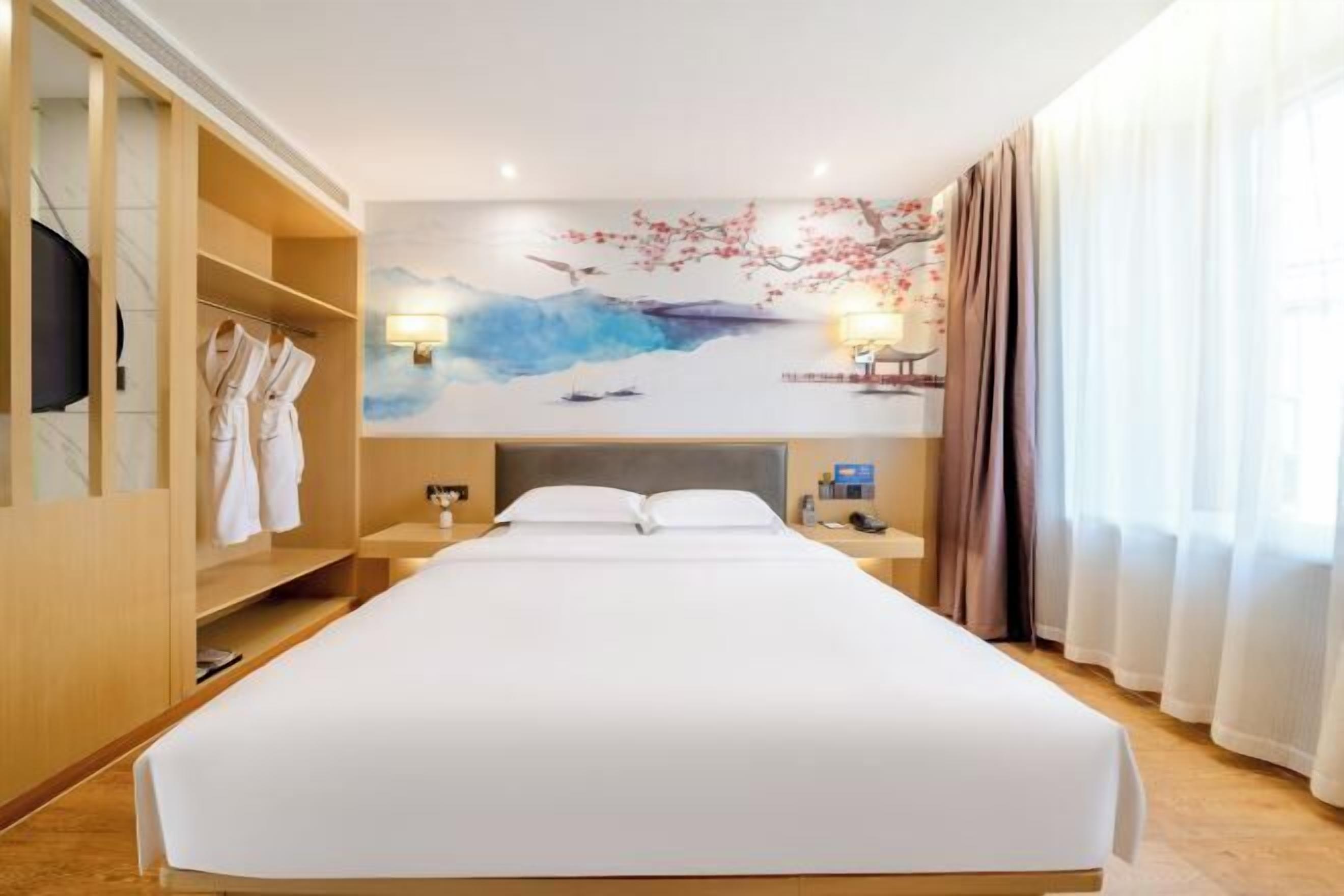 Une chambre d’hôtel avec un grand lit, une armoire, un tableau au mur, une table de chevet et une fenêtre avec des rideaux.