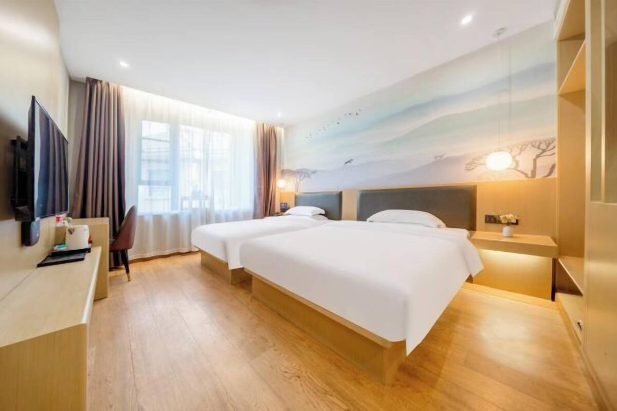A hotel room with two beds, a TV, a desk, and a painting on the wall.