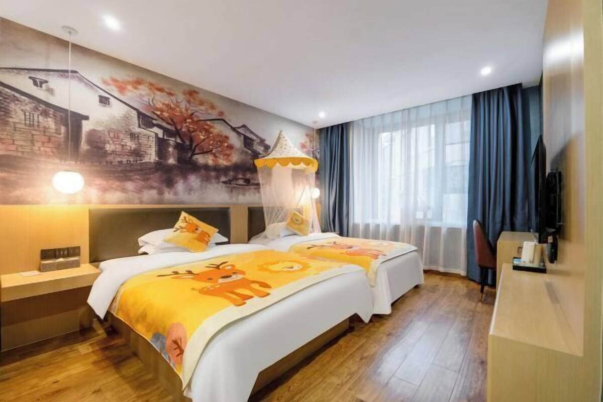 A hotel room with two beds, a mural on the wall, a desk with a lamp, and a TV.