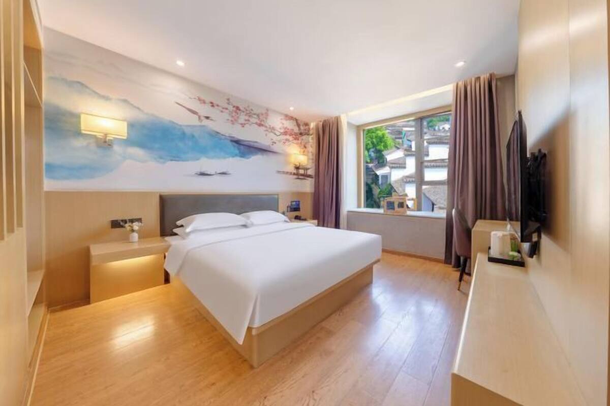 A hotel room with a large bed, a nightstand, a desk, a TV, and a window with curtains.