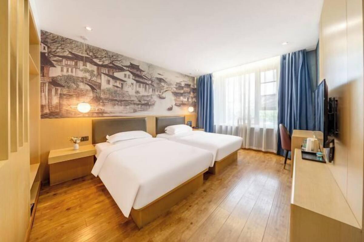 A hotel room with two beds, a mural, a desk, and a TV.