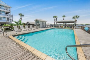 A pool area with a wooden deck, lounge chairs, and a small building. - Lagoon Landing 202- Beautifully Decorated Condo With Balcony Pool Steps to Beach Lagoon (Gulf Shores)