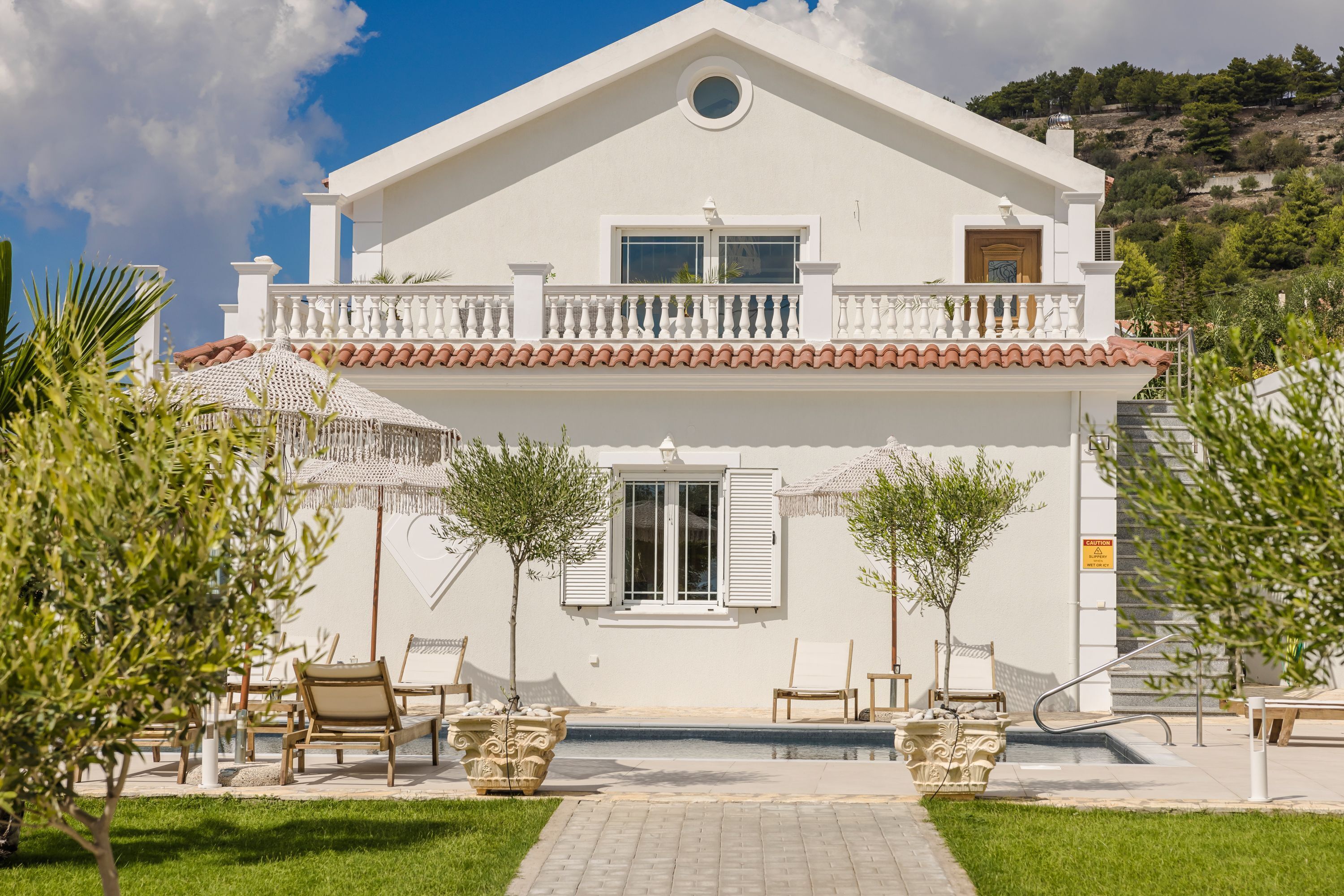 Un edificio blanco de dos pisos con balcón, piscina y mobiliario exterior.