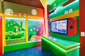 A brightly lit gaming area with a Nintendo Switch console, a wall with pixel art, and a green gaming center sign.
