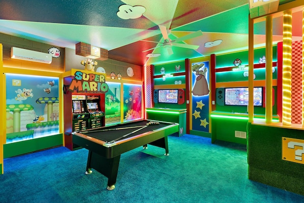 A colorful arcade room with a pool table, various gaming machines, and vibrant wall decorations.