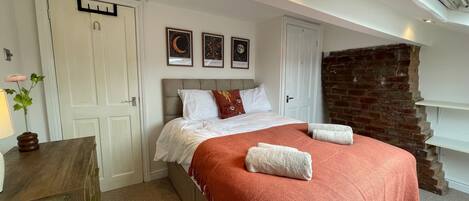 A bedroom with a bed, a wooden dresser, a brick wall, and a skylight.
