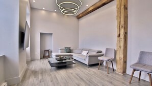 Un salon moderne avec un canapé gris, deux fauteuils, une table basse et une poutre en bois au plafond.