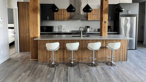 Une cuisine moderne dotée d’un îlot central, de tabourets de bar, d’appareils électroménagers en acier inoxydable et d’éléments décoratifs en bois.
