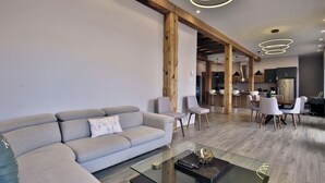 Un salon moderne avec un canapé d’angle, une table basse en verre et un coin repas comprenant une table et des chaises en bois.