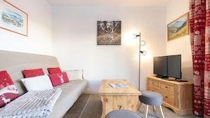 Ein modernes Hotelzimmer mit einer Couch, einem Holztisch, einem Fernseher und einem Schreibtisch mit Schubladen.