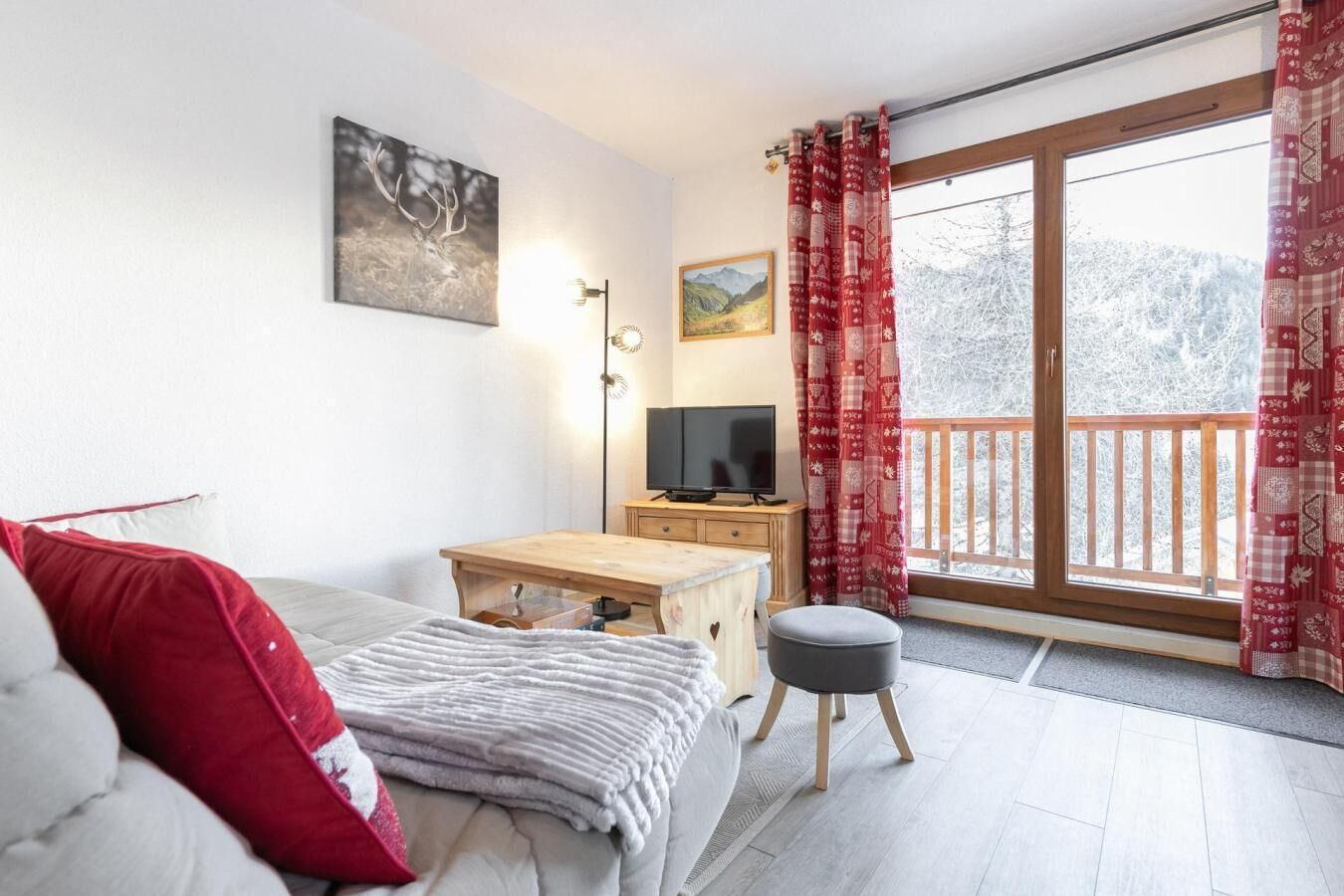 A cozy bedroom with a bed, a desk, a TV, and a balcony with red curtains.