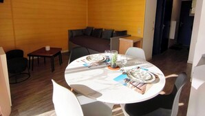 Een moderne eethoek met een ronde tafel voor vier personen, omringd door witte en zwarte stoelen. Achtergrond is een bank en een kleine tafel met één stoel.