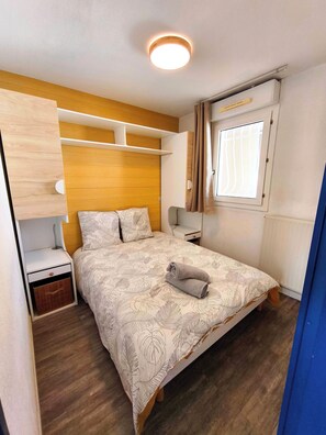 Un dormitorio con cama, mesitas de noche, armario, ventana con cortinas y lámpara en el techo.