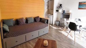 Een moderne leefruimte met een slaapbank, een klein houten tafeltje en een eethoek met stoelen.
