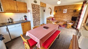 A cozy kitchen with wooden cabinets, a dining table with a checkered tablecloth, and a microwave. - 100m from ski slopes, 2nd floor, balcony, ski locker, 36m², Valfréjus (Valfréjus)