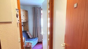 A narrow hallway leading to a bedroom with a bed, a window with curtains, and a door with a number plate. - 50m from ski slopes, 2nd floor, view mountain, balcony, tv, ski locker, 23m², Valfréjus (Valfréjus)