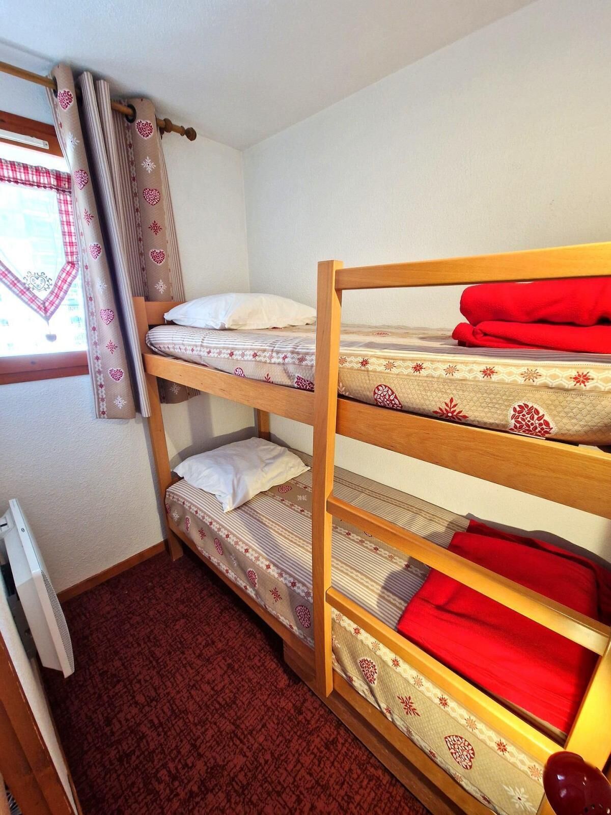 A bunk bed room with a window, curtains, and a radiator.