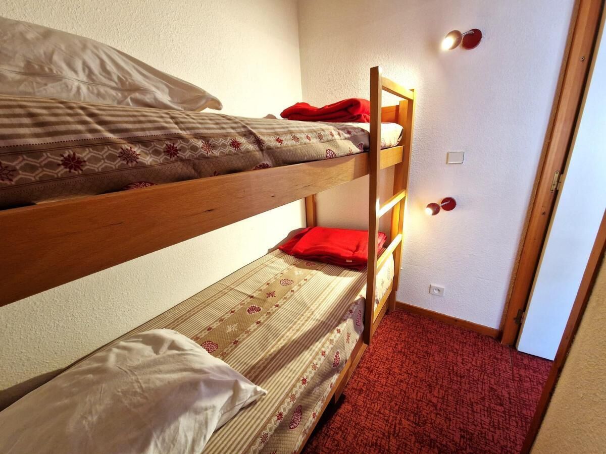 Habitación con literas, alfombra roja y una puerta con interruptor de luz.