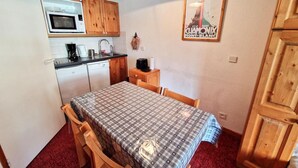 A compact kitchen with wooden cabinets, a microwave, and a coffee maker. There's a table with a checkered tablecloth and a poster on the wall. - 50m from ski slopes, 2nd floor, view mountain, balcony, tv, ski locker, 23m², Valfréjus (Valfréjus)