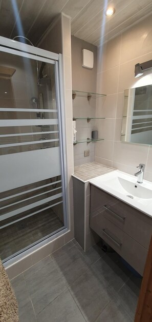 Uma casa de banho moderna com cabine de duche em vidro, lavatório branco e espelho.