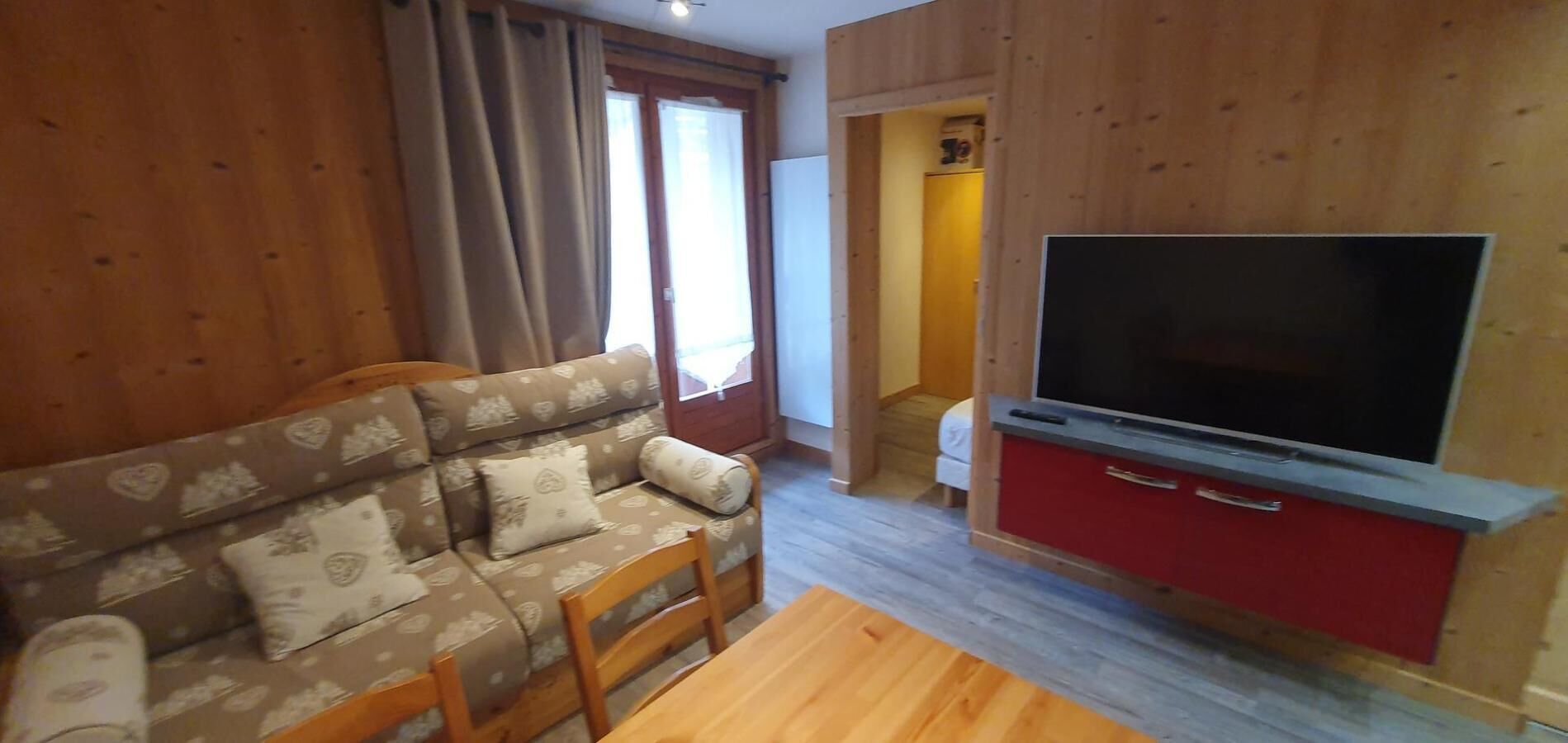 A cozy living room with a sofa, TV, and wooden floors.