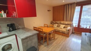 A compact kitchen with a washing machine, a dining table with chairs, and a sofa.
