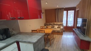 A compact kitchen with a dining area, a sofa, and a TV.