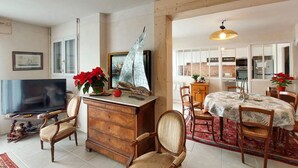 A living room with a TV, wooden furniture, a sailboat decoration, and a dining area with a table and chairs.