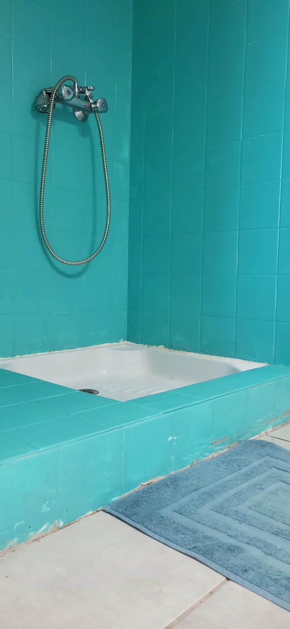 A bathroom with turquoise tiles, a bathtub, and a shower with a hose.